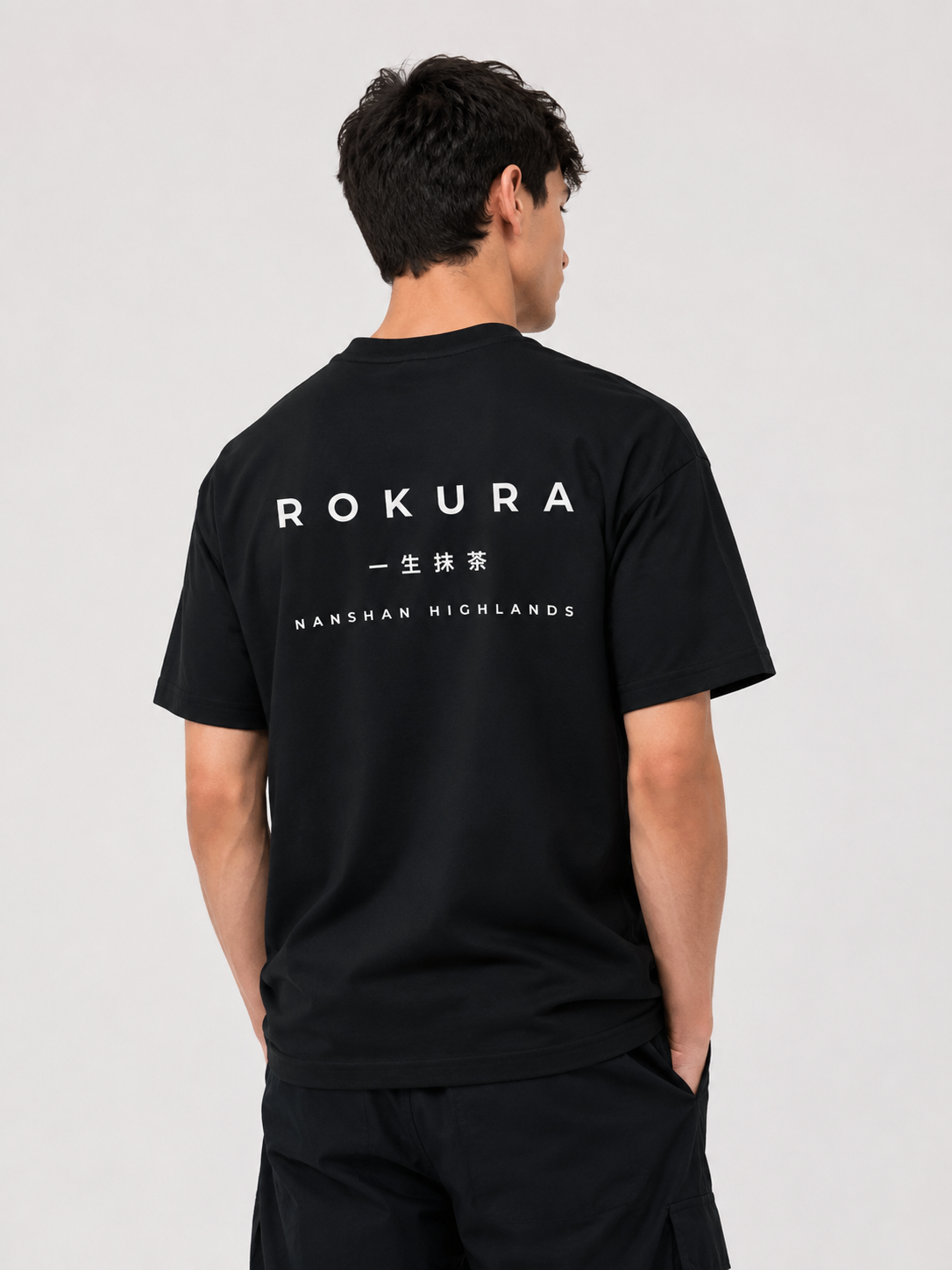 Back view of a man wearing the black ROKURA Nanshan Highlands oversized t-shirt with white graphic typography.