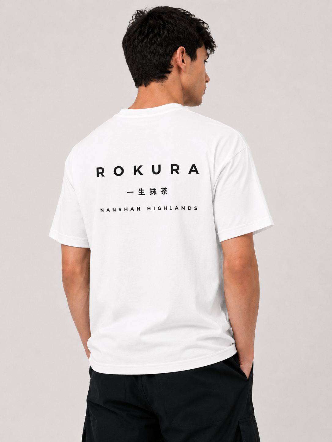 Back view of a man wearing the white ROKURA Nanshan Highlands oversized t-shirt with white graphic typography.