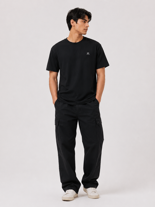 Full body view of a male model wearing the BLACK 6SENSE by ROKURA oversized t-shirt with relaxed black cargo trousers.
